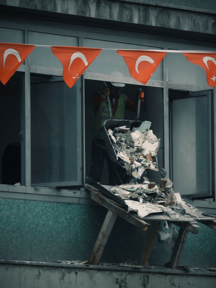 services-02 Worker throwing construction debris from a building window decorated with Turkish flags.